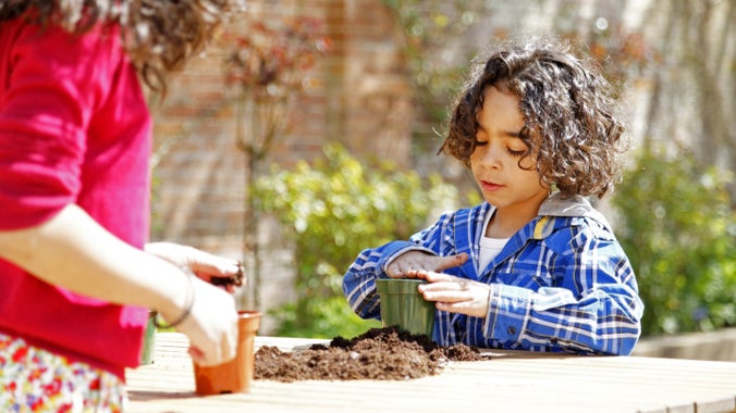 Children at a table planting seeds in flower pots at Mottisfont, Hampshire with shrubs in the background
